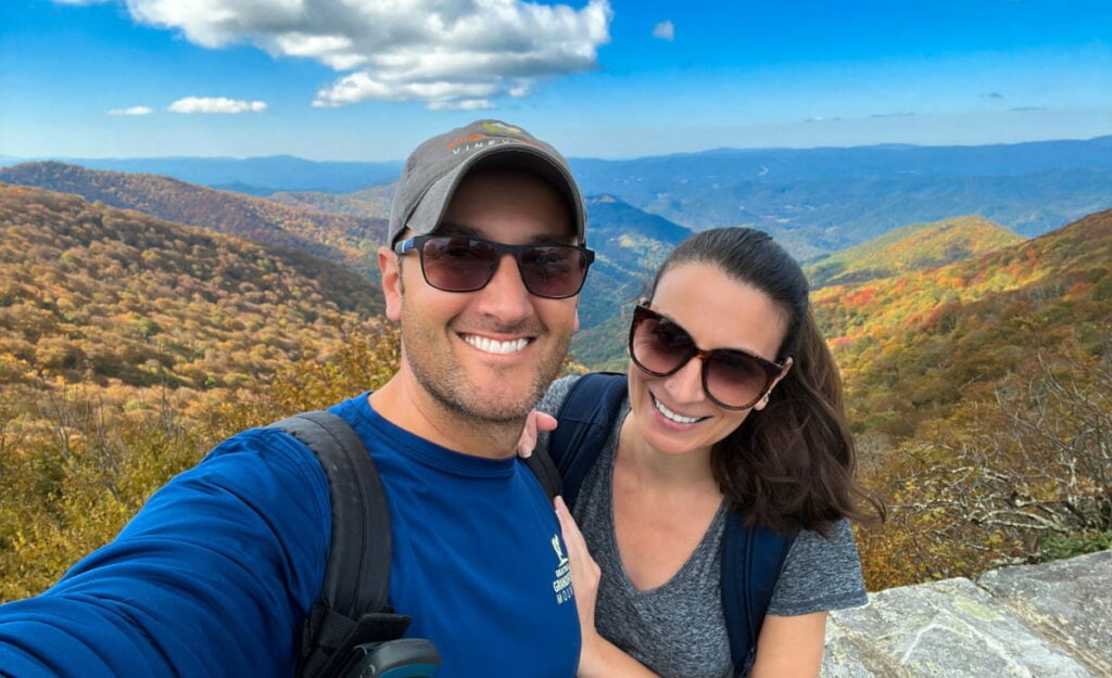 "36 Hours In Asheville Itinerary" featured article image with Tom and Christine, a white brunette male and female with sunglasses with beautiful Blue Ridge Mountains in the background at Craggy Gardens Visitor Center along the Blue Ridge Parkway