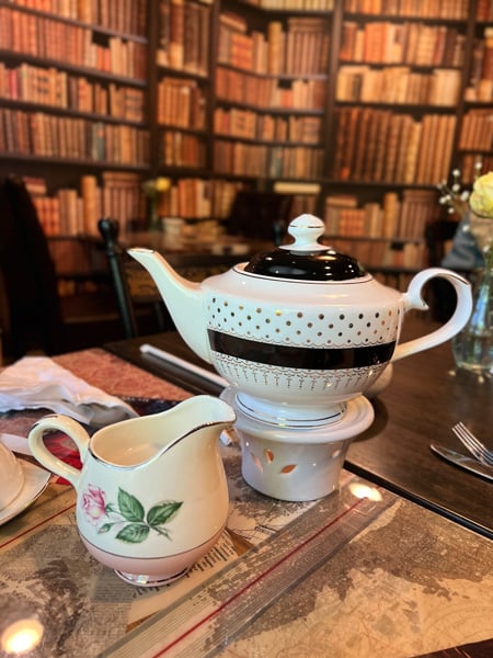 Book And Bee Cafe and Tea Hendersonville NC with black and white teapot next to creamer with pink flower on it on table with book wallpaper in the background