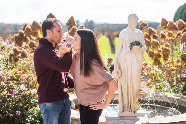 Christine and Tom, a brunette white male and female, drinking red and white wine in front of a fountain at Burntshirt Vineyards in Hendersonville, NC