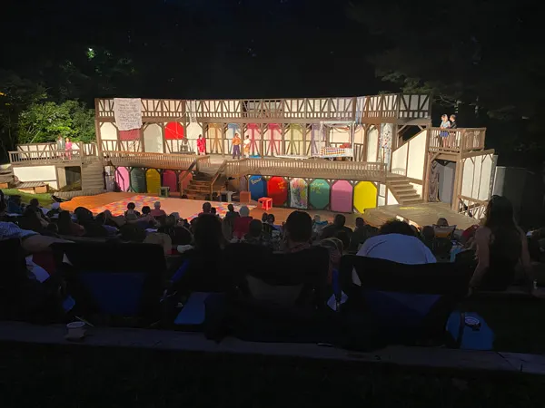 Montford Park Players Shakespeare in the Park with old fashioned stage lit up at night with people sitting in front