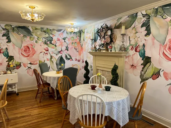 The Book And Bee Cafe Tearoom in Hendersonville with two tables with white table cloths and pink flowered wallpaper with white fireplace 