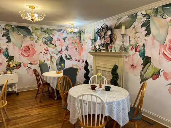 The Book And Bee Cafe Tearoom in Hendersonville with two tables with white table cloths and pink flowered wallpaper with white fireplace