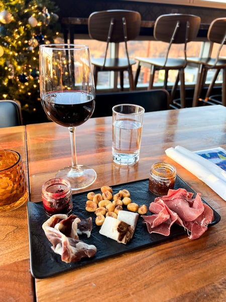Charcuterie board filled with meats, vegan cheese, and nuts with red glass of wine on table at The Montford Rooftop Bar in Asheville, NC