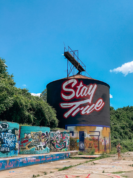 Asheville Silo with “Stay True” and graffiti on it in the Asheville River Arts District; Christine, a white brunette woman, is standing off to the side