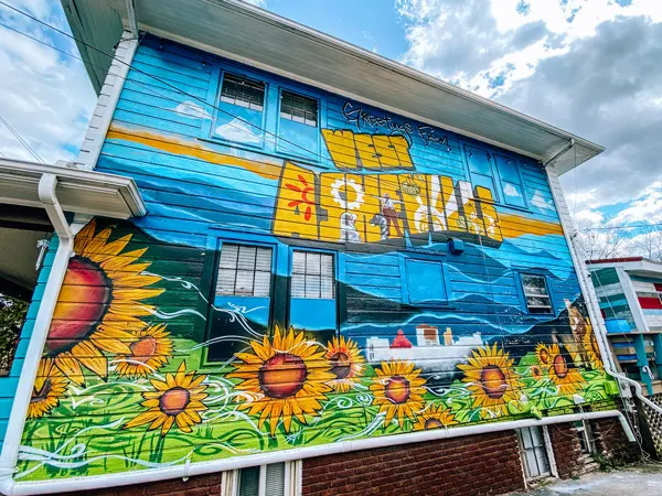 Best Neighborhoods In Asheville West Asheville Mural with house with welcome to West Asheville mural with blue sky and sunflowers