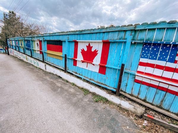 Bon Paul & Sharky's Hostel Country Flags mural with the United States and Canadian flags on a blue fence in West Asheville NC