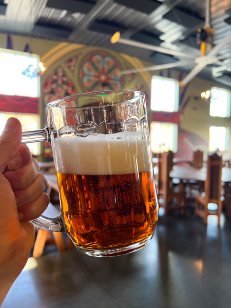 Burning Blush Brewery Mills River NC with white hand holding up amber beer in large glass beer mug in front of blurred taproom