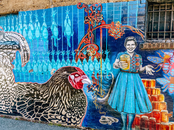 Chicken Alley Asheville mural with Sandra Gudger holding and selling honey next to chicken and rooster