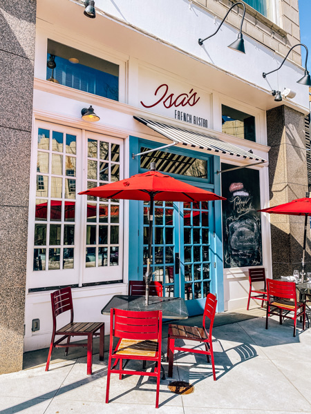 Haywood Park Hotel and Atrium Isa's Bistro with red chairs and umbrella at tables with bright blue doors against a white building