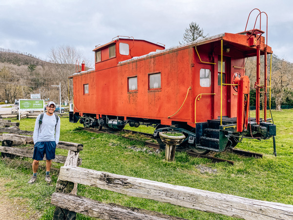 Lover's Leap Hike Loop Hot Springs NC with white brunette male with green backpack and hat standing in front of red caboose