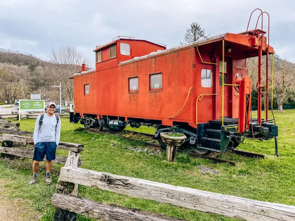 Lover's Leap Hike Loop Hot Springs NC with white brunette male with green backpack and hat standing in front of red caboose
