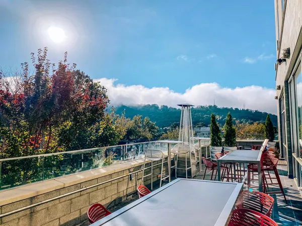 Ledge at Aloft Downtown Asheville NC Hotel with blue sky, fall foliage red trees, and outdoor patio with tables and chairs