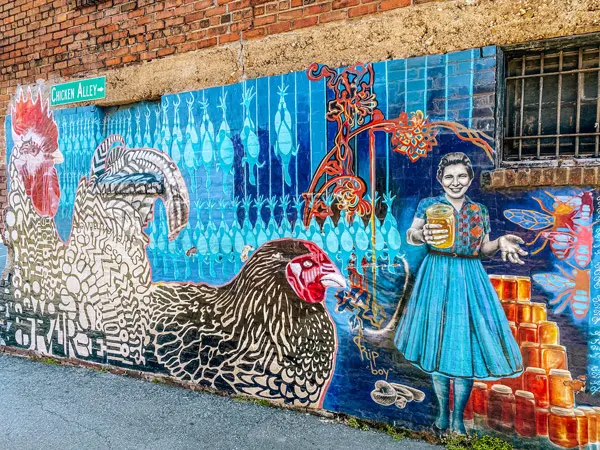 Molly Must Chicken Alley Mural Asheville NC with 10 foot rooster, chicken sitting down, and woman holding and selling jars of honey