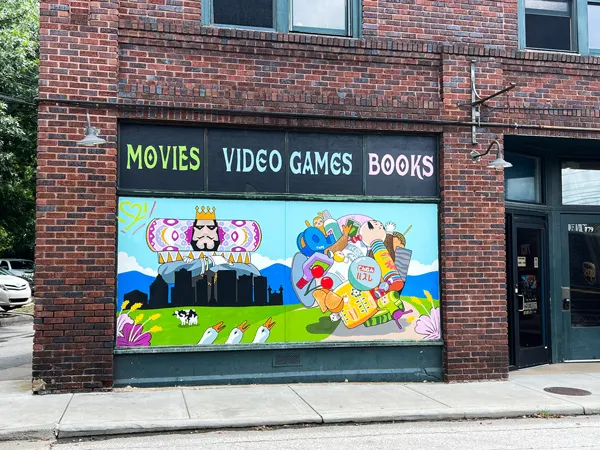 Orbit DVD West Asheville NC with colorful mural of king and video game like characters over cityscape with blue mountains