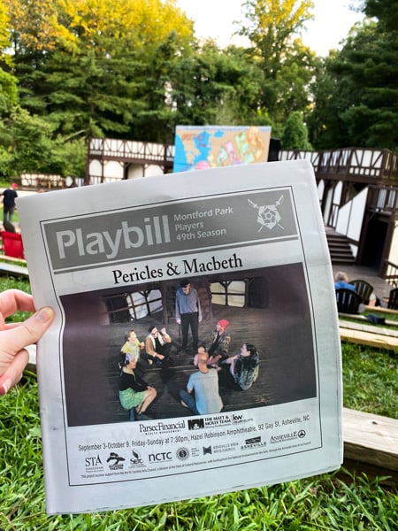 Christine’s white hand holding the playbill for Pericles and MacBeth in front of an outdoor stage at a Shakespeare in the Park performance in Asheville’s Historic Montford neighborhood