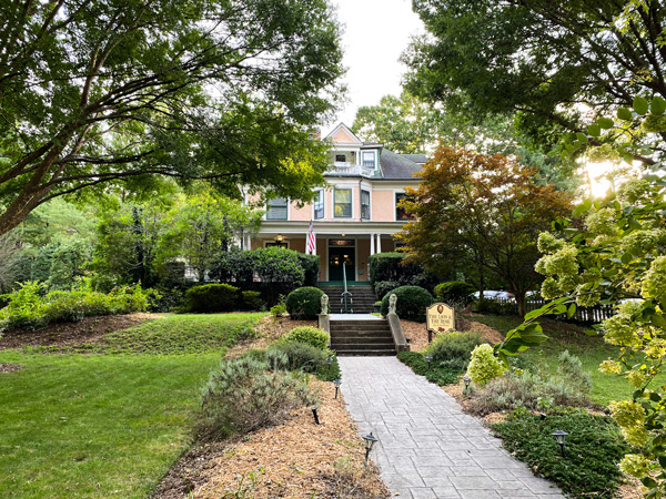 The Lion and the Rose Bed And Breakfast Montford NC with pink tan older home surrounded by trees and long sidewalk