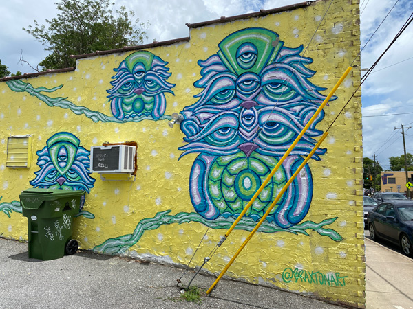 The Littlest Birds Asheville Mural with yellow background and green, blue and purple birds that look a bit like owls too