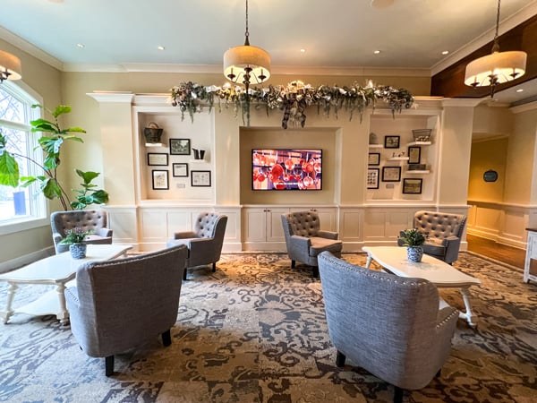 Village Hotel at Biltmore Estate in Asheville with lobby and lounge area with gray chairs, coffee tables, and TV with built in bookshelves