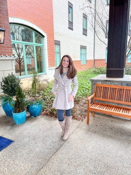 Village Hotel on Biltmore Estate in Asheville, North Carolina with white brunette female in pink coat, blue jeans, and gray boots standing outside at entrance