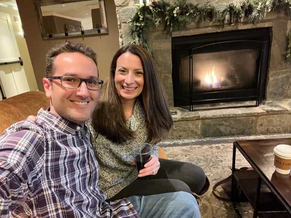 Village Hotel coffee and red wine from their Kitchen Cafe at Biltmore in Asheville with white brunette male and female on couch taking a selfie in front of lit gas fireplace