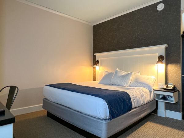 Village Hotel Room at Biltmore Estate in Asheville NC with white bed with blue accents and reading lights on either side with desk in front