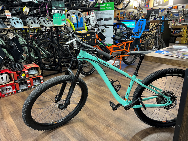 Asheville Bicycle Company with mountain bikes on floor, racks, and hanging from ceiling with turquoise-mint mountain bike up front