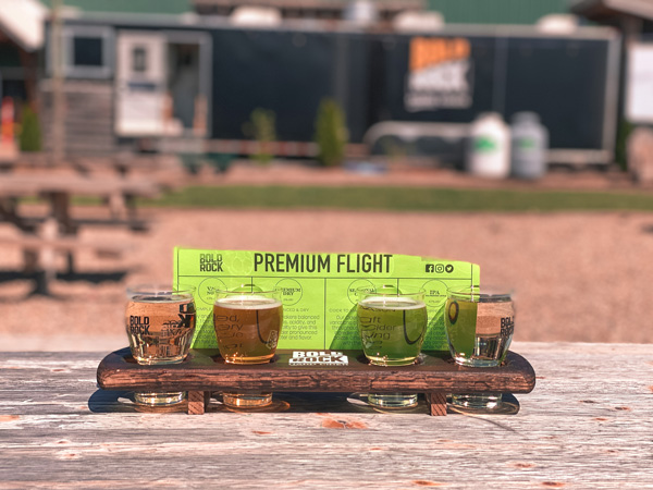 Bold Rock Cidery Mills River Premium Flight with four clear to light brown ciders in a flight with tasters and green paper naming the ciders