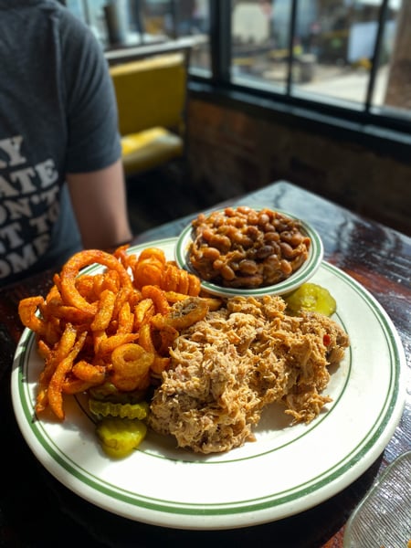 Buxton Hall BBQ Downtown Asheville NC with white plate filled with baked beans, seasoned french fries, pulled pork, and pickles