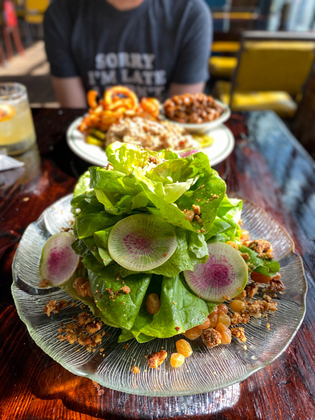 Buxton Hall Barbecue Asheville NC with large green salad with spiced pecans and radishes on clear plate and BBQ dish blurred in background