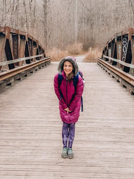 Daniel Ridge Loop with white brunette woman in garnet colored winter coat with hood and purple hiking leggings standing on a bridge