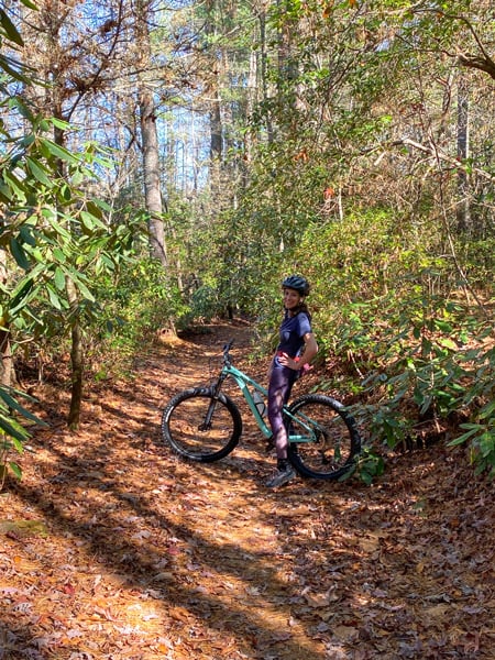 Explorer Trail Bent Creek Experimental Forest Asheville NC with white brunette female on mint colored mountain bike on dirt trail surrounded by fall foliage trees