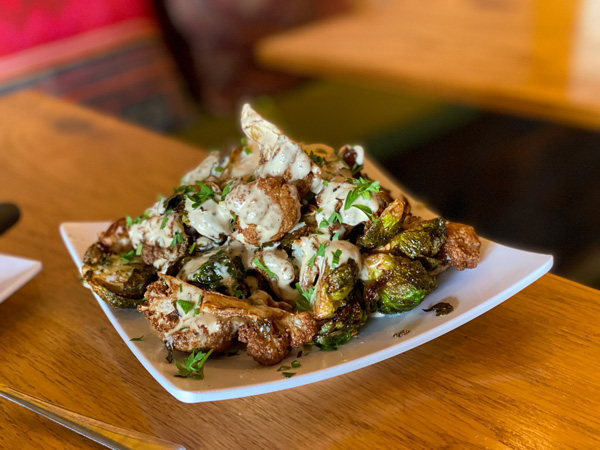 Gypsy Queen Cuisine Vegan restaurant Asheville, NC with plate of fried Brussels and cauliflower with sauce