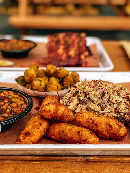 Luellas BBQ Asheville NC with pulled pork, hush puppies, fried okra, and black eyed peas on platter with BBQ ribs and baked beans blurred in background
