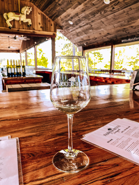 Parker Binns Vineyard Tryon Foothills NC with wine tasting glass under covered outdoor seating and bar with menus and wine bottles