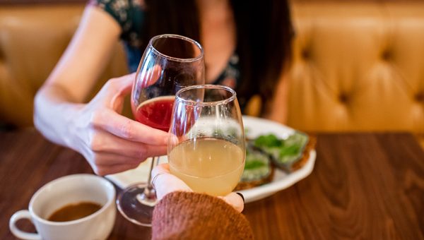 Tupelo Honey Asheville NC with white brunette woman doing a red and orange mimosa cheers with plate of avocado toast