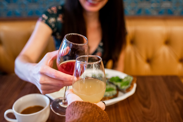 Tupelo Honey Asheville NC with white brunette woman doing a red and orange mimosa cheers with plate of avocado toast