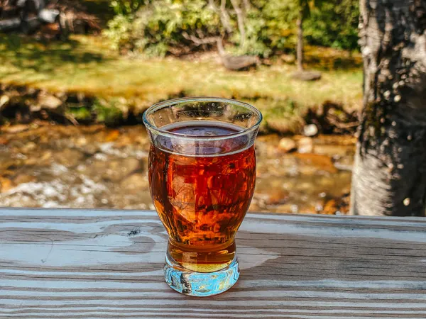 Bearwaters Brewing Company Maggie Valley NC with beer flight glass filled with amber colored ale sitting on a railing with river in the background
