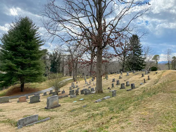 Historic Riverside Cemetery Montford with picture of rolling green hill, blue sky, a bare tree, and gravestones