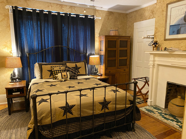 Inn Around The Corner Black Mountain Bed and Breakfast with bed with star bedspread, fireplace, and dresser in an older home with blue curtains behind the bed