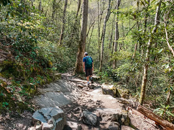 Mingo Falls Pigeon Creek Trail NC with white brunette male wearing green backpack hiking along rocks in forest
