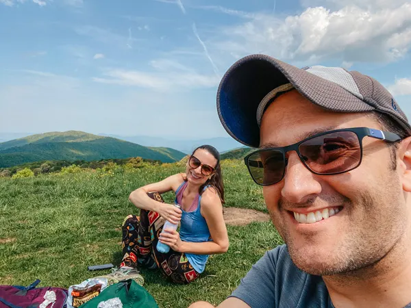 Picnic On Max Patch Summit with brunette white male and female hikers sitting on the ground with lunch
