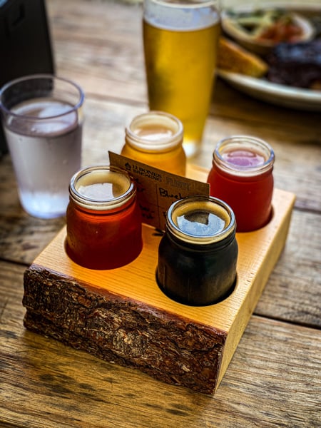 12 Bones Smokehouse Brewery South Asheville beer flight with four small glasses filled with a stout, 2 ambers, and yellow beer on brown picnic table