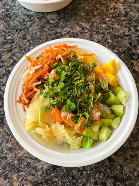 Aloha Cafe in Asheville NC Poke Bowl with carrots, mango, cilantro, and ginger on white rice with raw salmon in takeaway white bowl