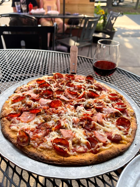 Asheville Brewing Company in Asheville NC Pizza on tin tray outside with glass of red wine - and some pizza toppings include pepperoni, vegan cheese, and ham