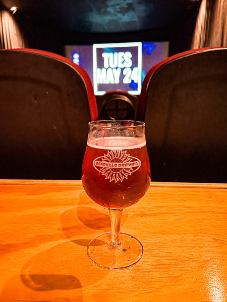 Asheville Brewing Company Theater in Asheville, NC with amber beer in logo glass on table with theater seats and movie screen in the background