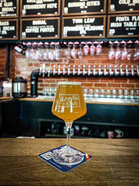 Asheville Club Bar with light colored beer in glass on bar counter with taps and draft list in background