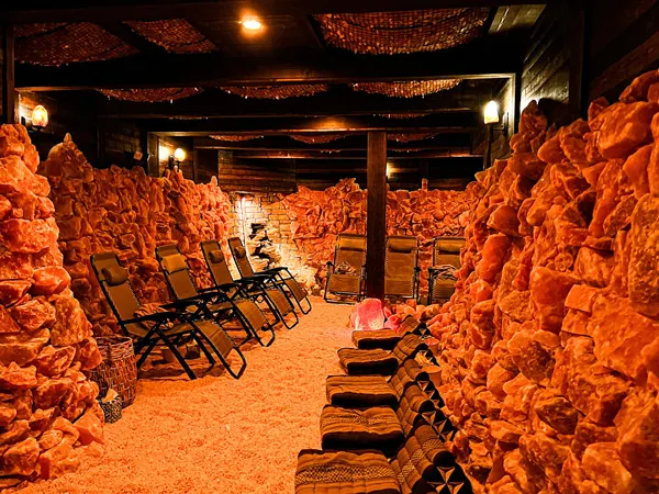 Asheville Salt Cave Community Room with orange lighting and walls, ground, and ceiling covered with pink salt with zero gravity chairs to sit in