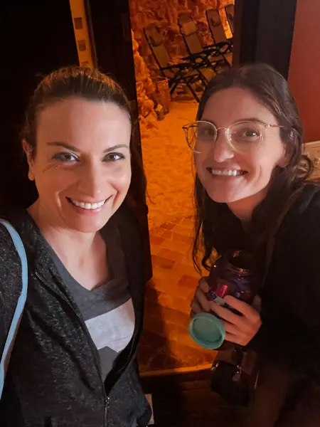Asheville Salt Cave in North Carolina with two white brunette women taking selfie in front of the community salt cave which has orange lighting