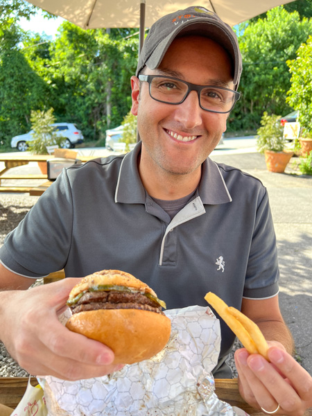Baby Bull Asheville NC Restaurant with white brunette male with glasses and hat in gray shirt holding up gluten free Burger and fries