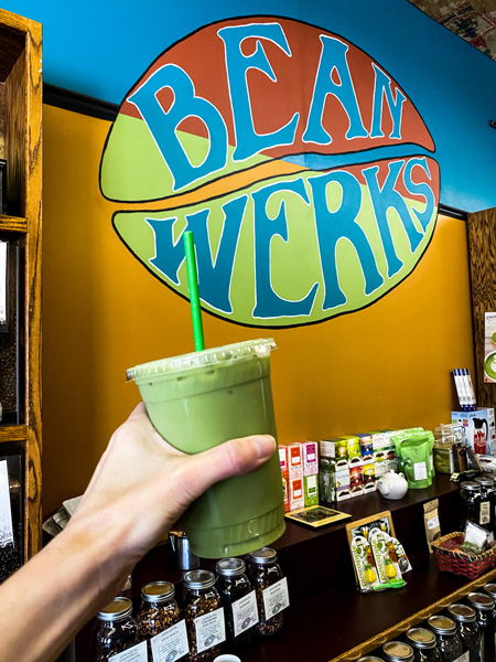 Bean Werks Coffee West Asheville with green tea latte in front of Bean Werks green, orange, and yellow logo